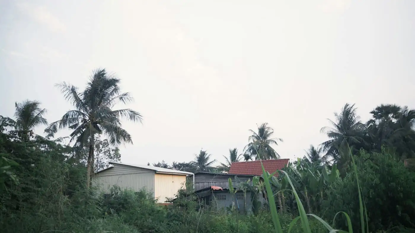 Overgrown flat kampung lot with banana trees and a wire fence before construction